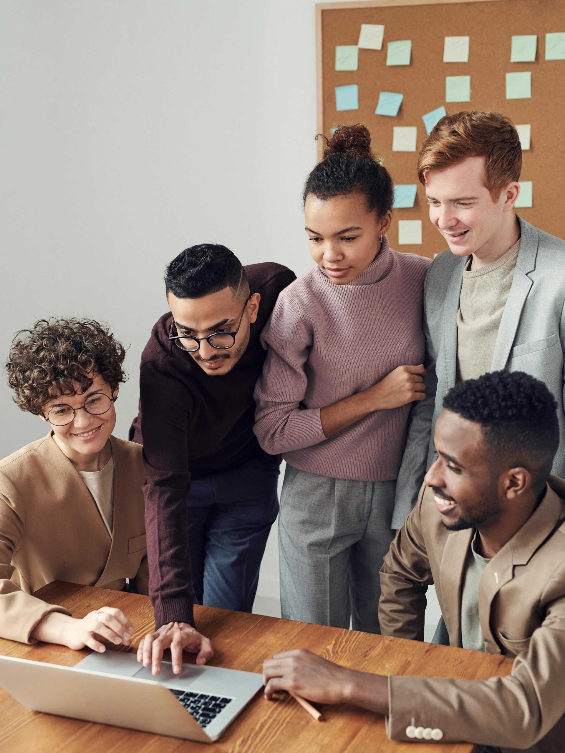 A diverse group of young professionals collaborating around a laptop in a modern office setting.